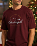 Man wearing a maroon t-shirt with Christmas-themed text in a festive indoor setting.